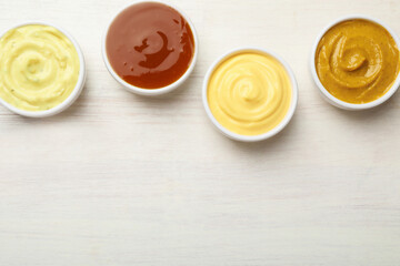 Different tasty sauces in bowls on white wooden table, flat lay. Space for text