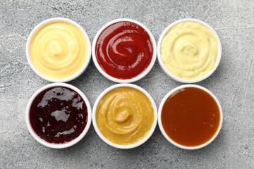 Different tasty sauces in bowls on grey table, flat lay