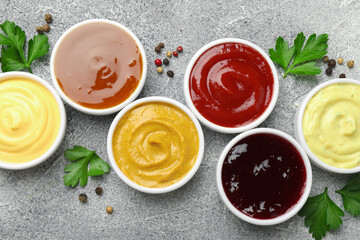 Different tasty sauces in bowls, parsley and peppercorns on grey table, flat lay