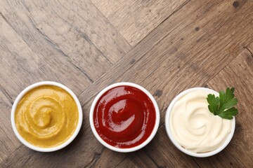 Different tasty sauces in bowls and parsley on wooden table, flat lay. Space for text