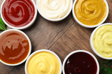 Frame made of different tasty sauces in bowls and parsley on wooden table, flat lay. Space for text