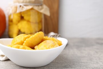 Pickled pattypan squashes in bowl on grey textured table against white background, closeup. Space for text