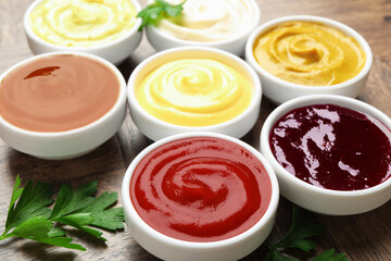 Different tasty sauces in bowls and parsley on wooden table, closeup