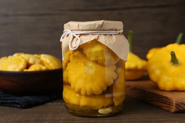 Pickled pattypan squashes in glass jar on wooden table, closeup
