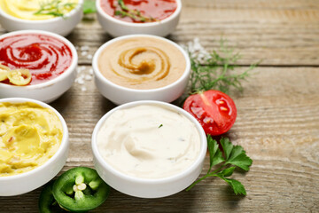 Different sauces and herbs on wooden table, closeup