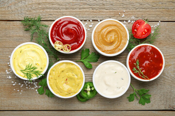Different sauces and herbs on wooden table, flat lay