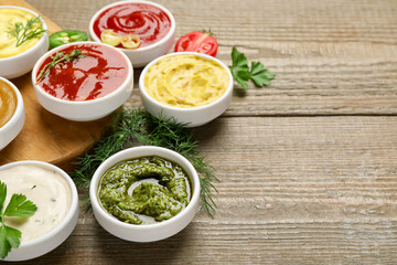 Different sauces and herbs on wooden table, closeup. Space for text