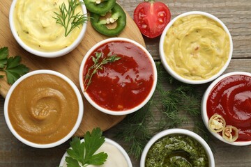 Different sauces and herbs on wooden table, flat lay
