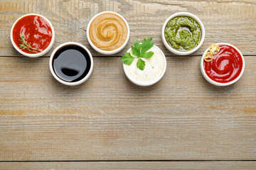 Different sauces and parsley on wooden table, flat lay. Space for text