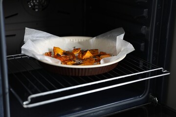 Baking dish with pieces of pumpkin and thyme in oven, closeup