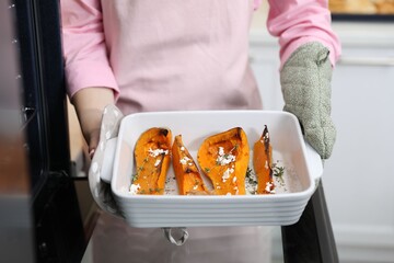 Woman with tasty baked pumpkin near oven indoors, closeup