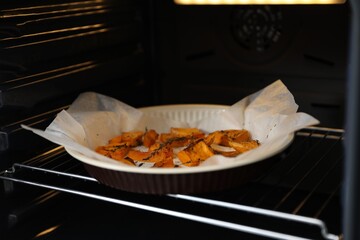 Baking dish with pieces of pumpkin and thyme in oven, closeup