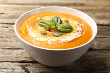 Delicious pumpkin cream soup with basil and seeds served on wooden table, closeup