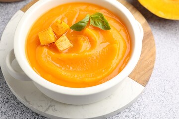 Delicious pumpkin cream soup with basil served on grey table, closeup