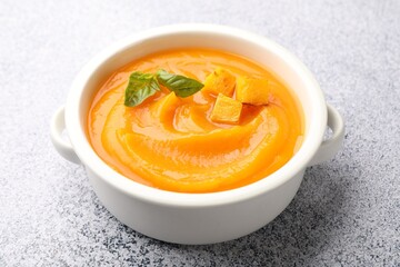 Delicious pumpkin cream soup with basil served on grey table, closeup