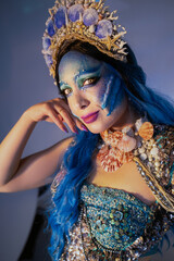 Portrait of an attractive woman with mermaid makeup, blue hair, and a seashell crown.