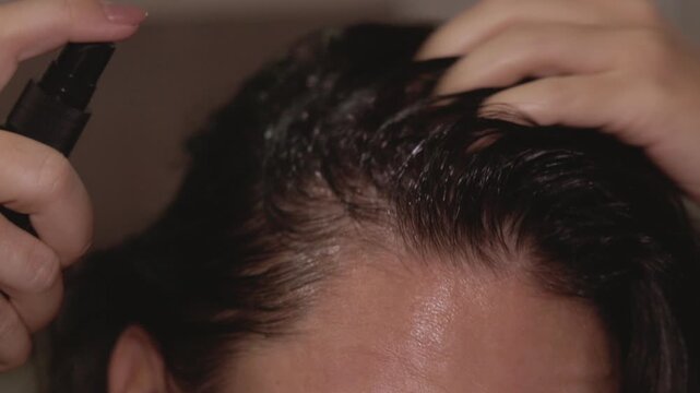 Woman in bathroom applying hair oil and spray for growth and strength. Half of her face visible, focusing on hair care routine. Castor and rosemary oil treatment for healthy shiny roots and hair loss 