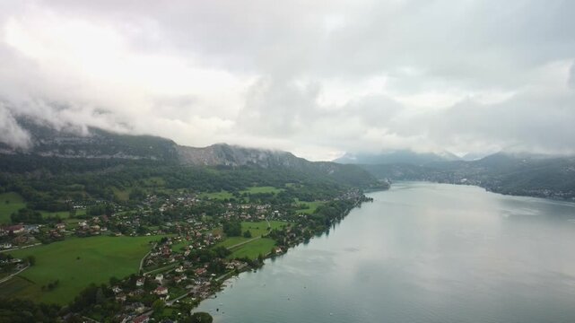 Lake Annecy, drone video captures the surrounding town of Chaperon with low lying clouds on mountains behind. The footage slowly drops showing the stunning views in particular the beautifully lake.