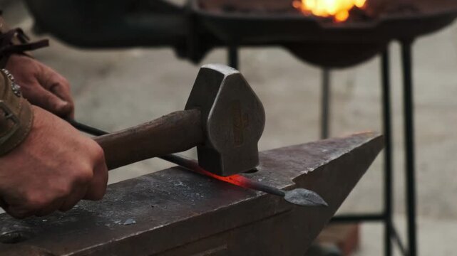 High-angle static close-up of a blacksmith hammering a red-hot spearhead on an anvil; glowing steel and precise strikes in a gritty workshop backdrop.