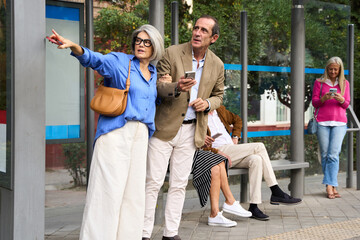 Senior couple waiting at bus stop using phone