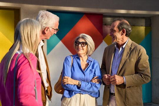Senior friends enjoying conversation outdoors against colorful wall - Powered by Adobe