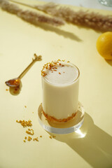Milk drink with honey and flowers. Milk drink with honey and edible flowers on yellow background, healthy floral beverage concept