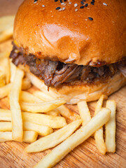 Pulled pork burger with french fries on wooden board.