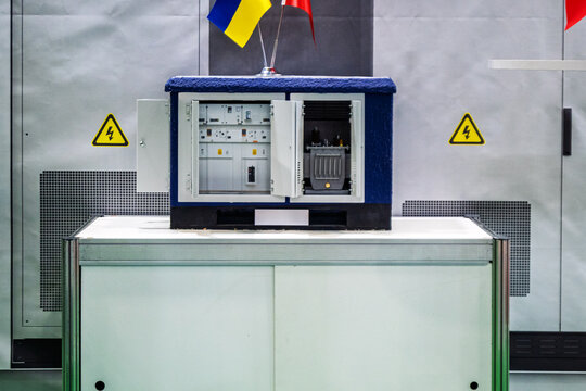 Compact electrical transformer substation model with open doors, showcasing internal components and safety signs. Features Ukrainian flag, symbolizing energy infrastructure and technology on display,