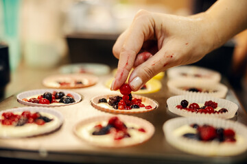 Hand placing fresh berries on baking muffins