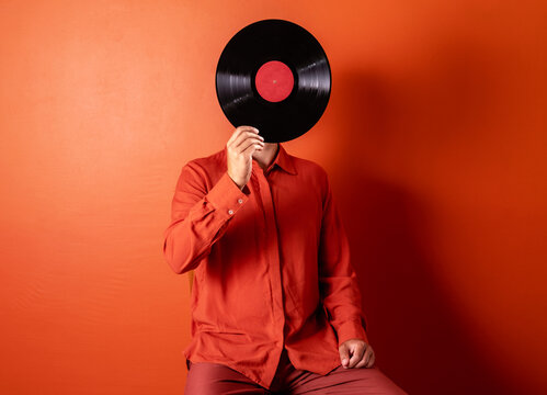 Man holding vinyl record covering face in orange studio