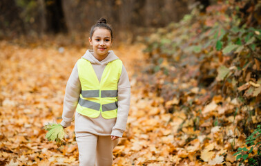 Little girl wearing  reflective vest smiling looking to the camera otdoors.