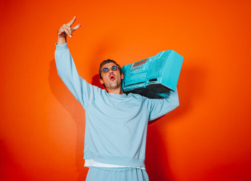 Man in blue outfit holding boombox against orange background having fun