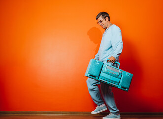 Man with blue boombox in front of orange wall in casual retro style