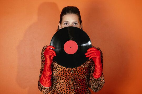 Portrait of woman in leopard print holding vinyl record in red gloves