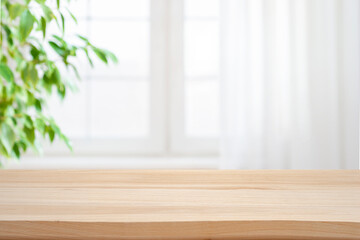 Empty wooden table against blurred window with curtain and green pant branch background