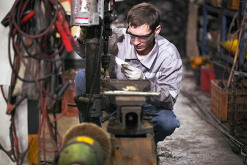 White man technician checking used car damaged engine block at scrap yard warehouse recycle area part. Maintenance engineer inspecting rust oily auto motor old spare part in junkyard for reuse service