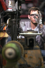 White man technician checking used car damaged engine block at scrap yard warehouse recycle area part. Maintenance engineer inspecting rust oily auto motor old spare part in junkyard for reuse service