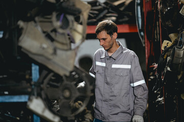 White man technician checking used car damaged engine block at scrap yard warehouse recycle area part. Maintenance engineer inspecting rust oily auto motor old spare part in junkyard for reuse service