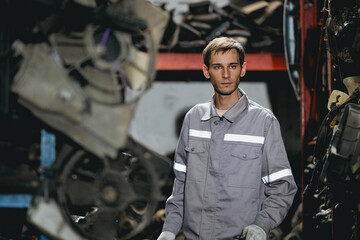 White man technician checking used car damaged engine block at scrap yard warehouse recycle area part. Maintenance engineer inspecting rust oily auto motor old spare part in junkyard for reuse service