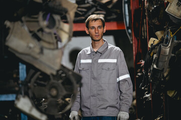 White man technician checking used car damaged engine block at scrap yard warehouse recycle area part. Maintenance engineer inspecting rust oily auto motor old spare part in junkyard for reuse service