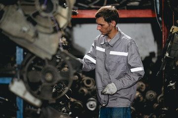 White man technician checking used car damaged engine block at scrap yard warehouse recycle area part. Maintenance engineer inspecting rust oily auto motor old spare part in junkyard for reuse service