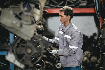 White man technician checking used car damaged engine block at scrap yard warehouse recycle area part. Maintenance engineer inspecting rust oily auto motor old spare part in junkyard for reuse service
