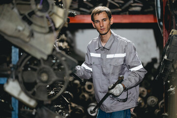 White man technician checking used car damaged engine block at scrap yard warehouse recycle area part. Maintenance engineer inspecting rust oily auto motor old spare part in junkyard for reuse service