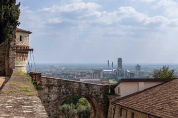 Fototapeta premium Panoramic view of Brescia from the castle walls, looking through the stone arch of old bridge toward the city modern skyline