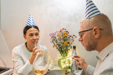 Party Couple Celebrating Birthday Indoor; Drinks, Flowers, Happiness. Intimate birthday celebration indoors; a couple enjoys drinks and flowers.