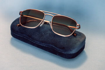 Modern designer sunglasses with metallic frame and gradient tinted glass, placed on an elegant navy velvet case against soft pastel backdrop