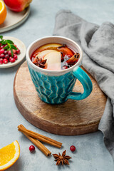 A mulled wine in a mug with cinnamon, cranberry and fruits on a wooden board on a light background
