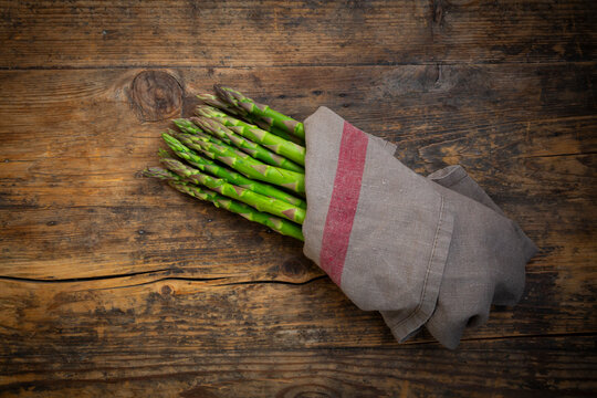 Fresh green asparagus wrapped in kitchen towel on rustic wood