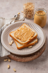 Peanut butter toast on a plate on a light background with scattered nuts, spread and napkin.
