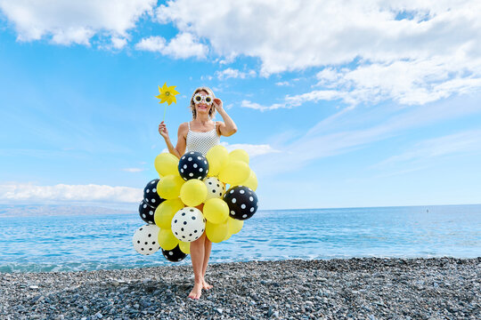 Woman dressed in polka dot balloons on a sunny Mediterranean pebble beach